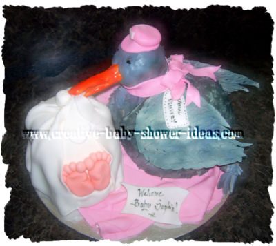 grey carved stork shower cake with pink scarf and baby wrapped in white blanket