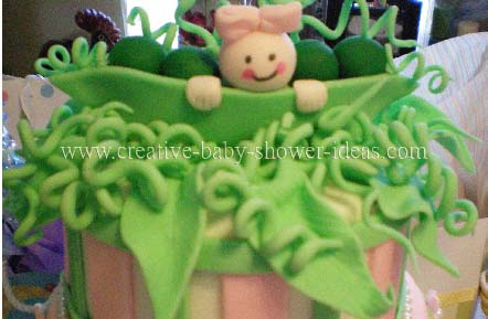 closeup of top of pea in pod cake with smiling baby and pink bow on her head